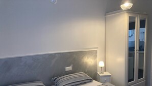 A bedroom with two beds, a bedside table with a lamp, and a wardrobe with glass doors.