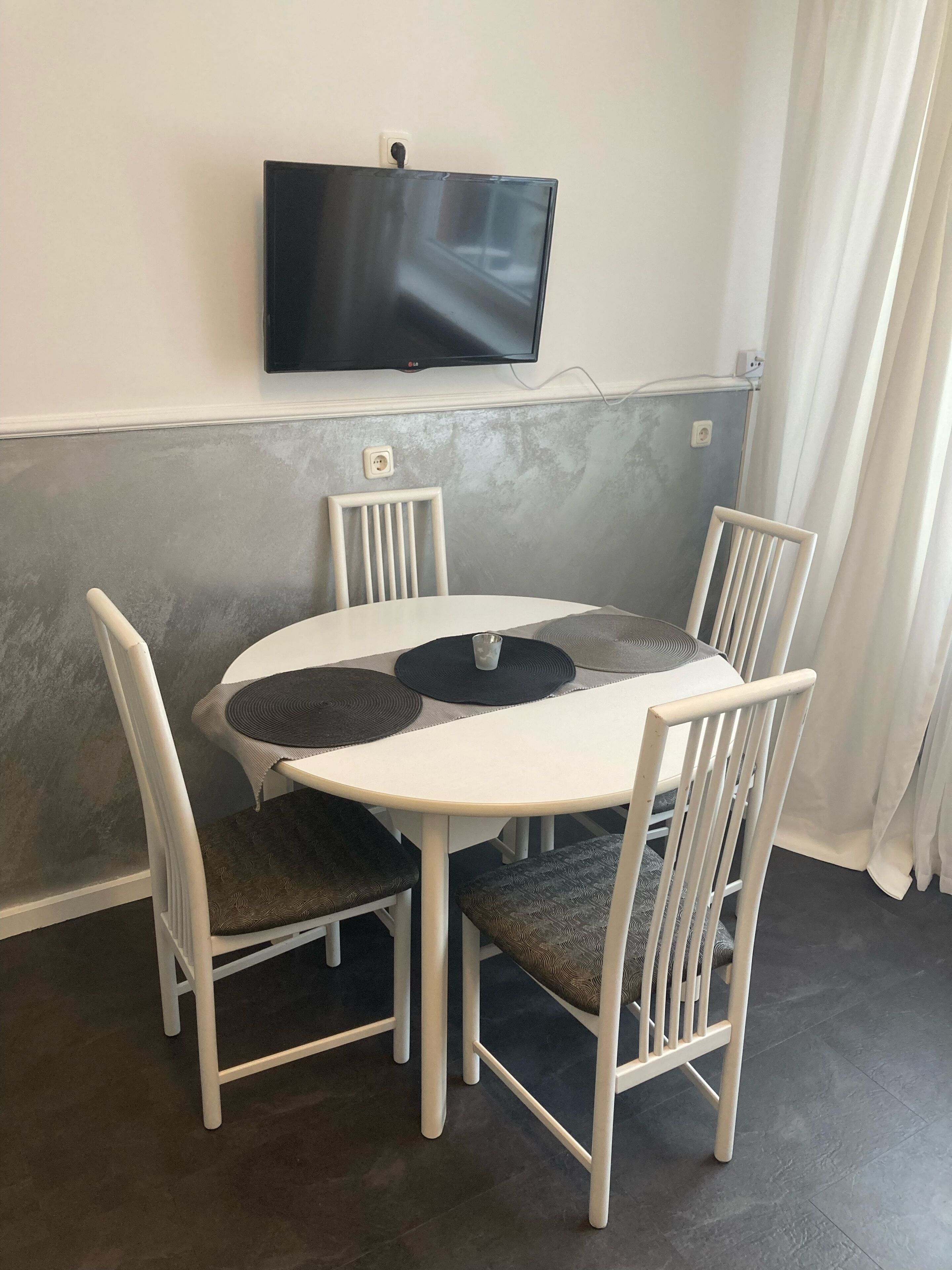 Un coin repas comprenant une table ronde, quatre chaises, un téléviseur à écran plat fixé au mur et une prise de courant.