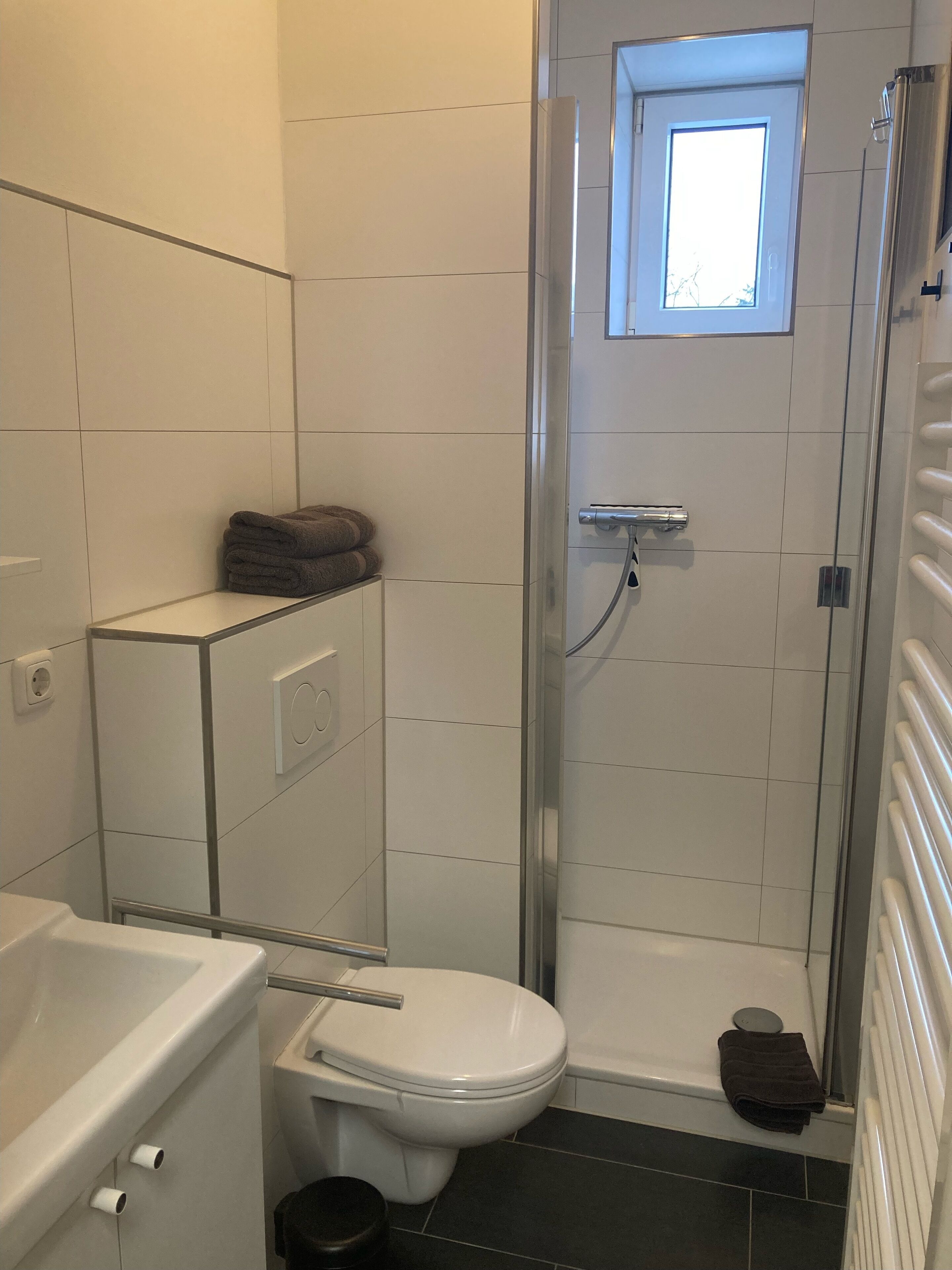 Une salle de bain comprenant des toilettes, une douche avec une porte en verre et une petite fenêtre située au-dessus de la douche.