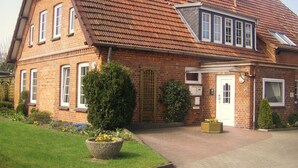 A two-story brick house with a sloped roof, a front porch, and a well-maintained garden.