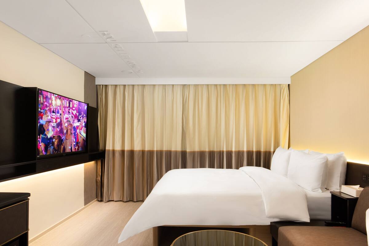 Ein Hotelzimmer mit Bett, Fernseher, Nachttisch, Sessel und kleinem Tisch.