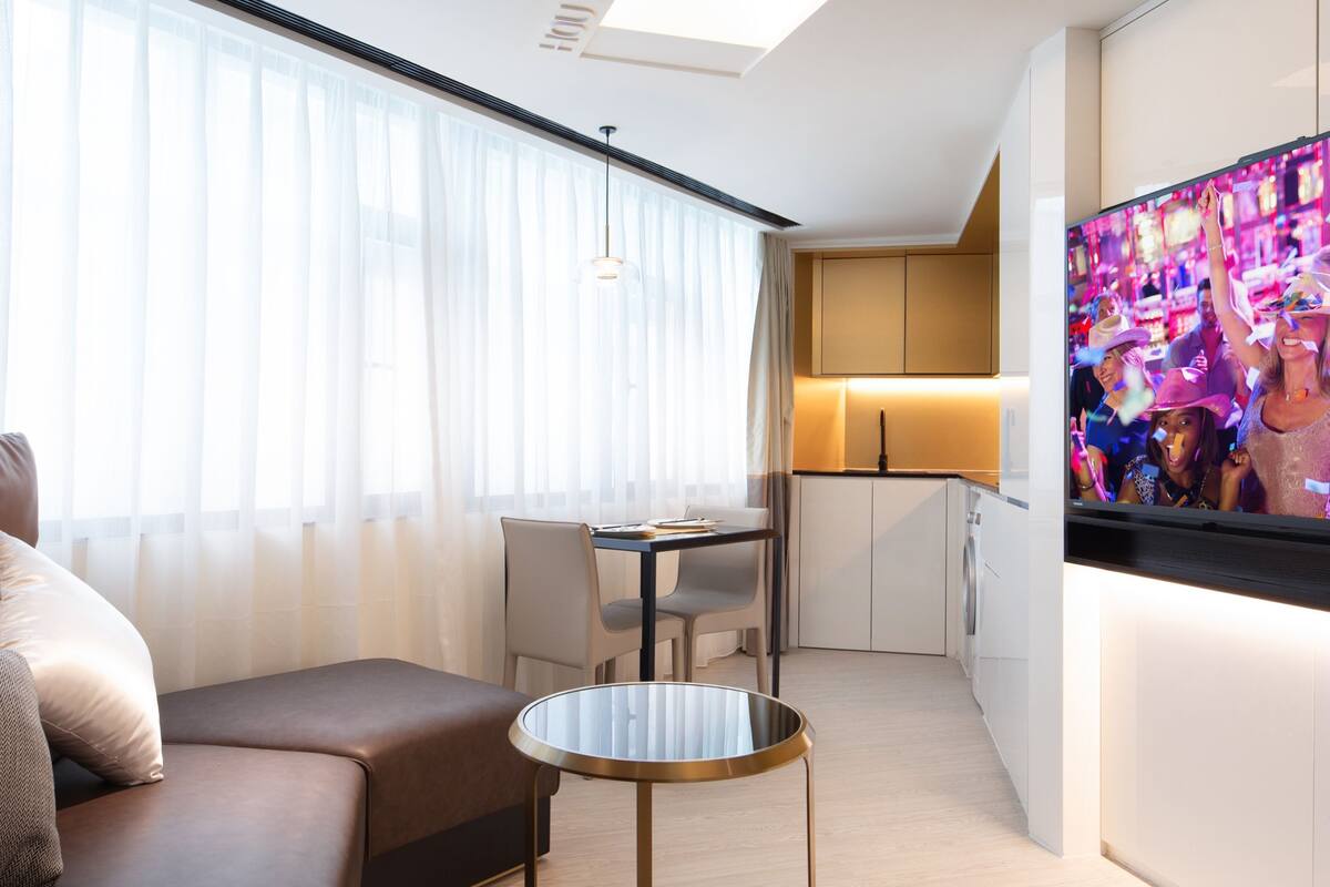 Ein modernes Hotelzimmer mit einer Sitzecke, einem kleinen runden Tisch, einem Fernseher und einer Küchenzeile.