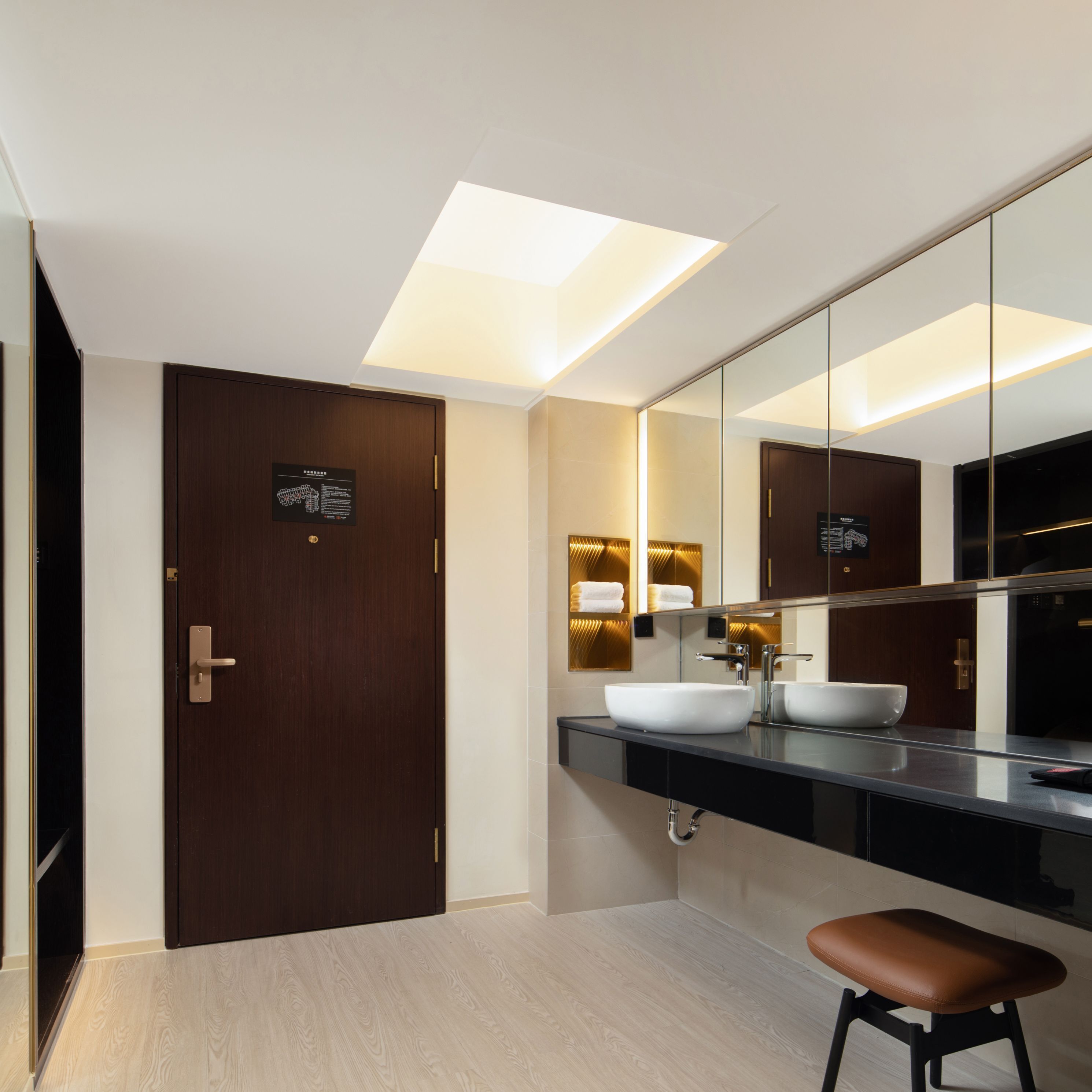 A modern bathroom with a dark wooden door, a large mirror, and a white sink.
