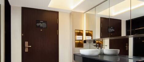 A modern bathroom with a dark wooden door, a large mirror, and a white sink.