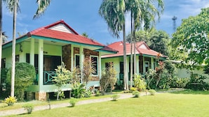 A two-story building with a red roof and green walls, surrounded by lush greenery and palm trees. - Swiss Chalet Garden Pool Resort (Krabi)