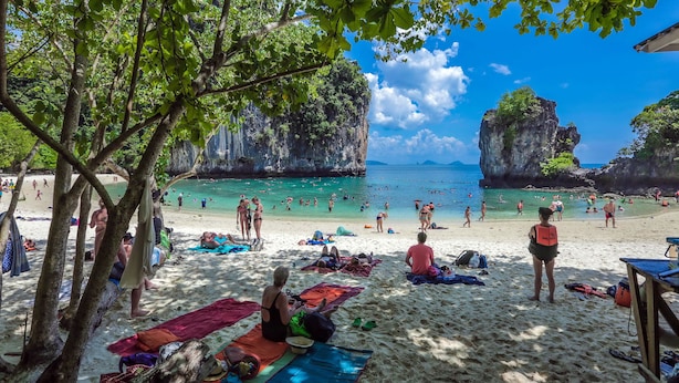 A beach with people sunbathing and swimming, surrounded by rocky cliffs and trees. - Swiss Chalet Garden Pool Resort (Krabi)