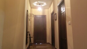 Un pasillo con una puerta de madera al final, una lámpara en el techo y un perchero en la pared.