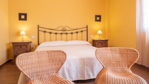 Una habitación con una cama, dos mesitas de noche, dos lámparas de pared y dos sillas de mimbre.