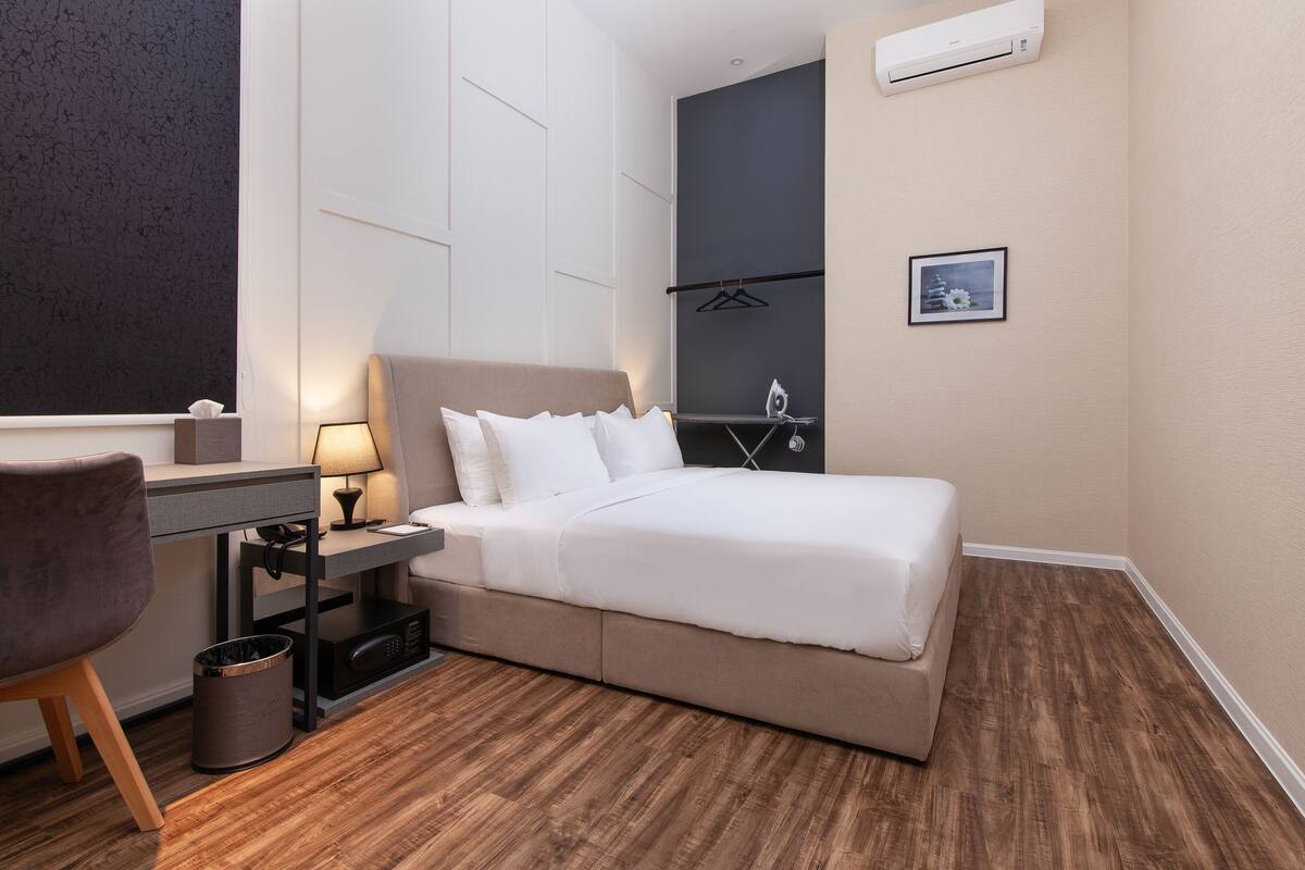 A hotel room with a bed, desk, chair, and a small trash bin.