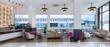Un lobby espacioso con un diseño moderno, que incluye una zona de estar con sofás y sillones, un mostrador de recepción y grandes ventanales con vistas al exterior.