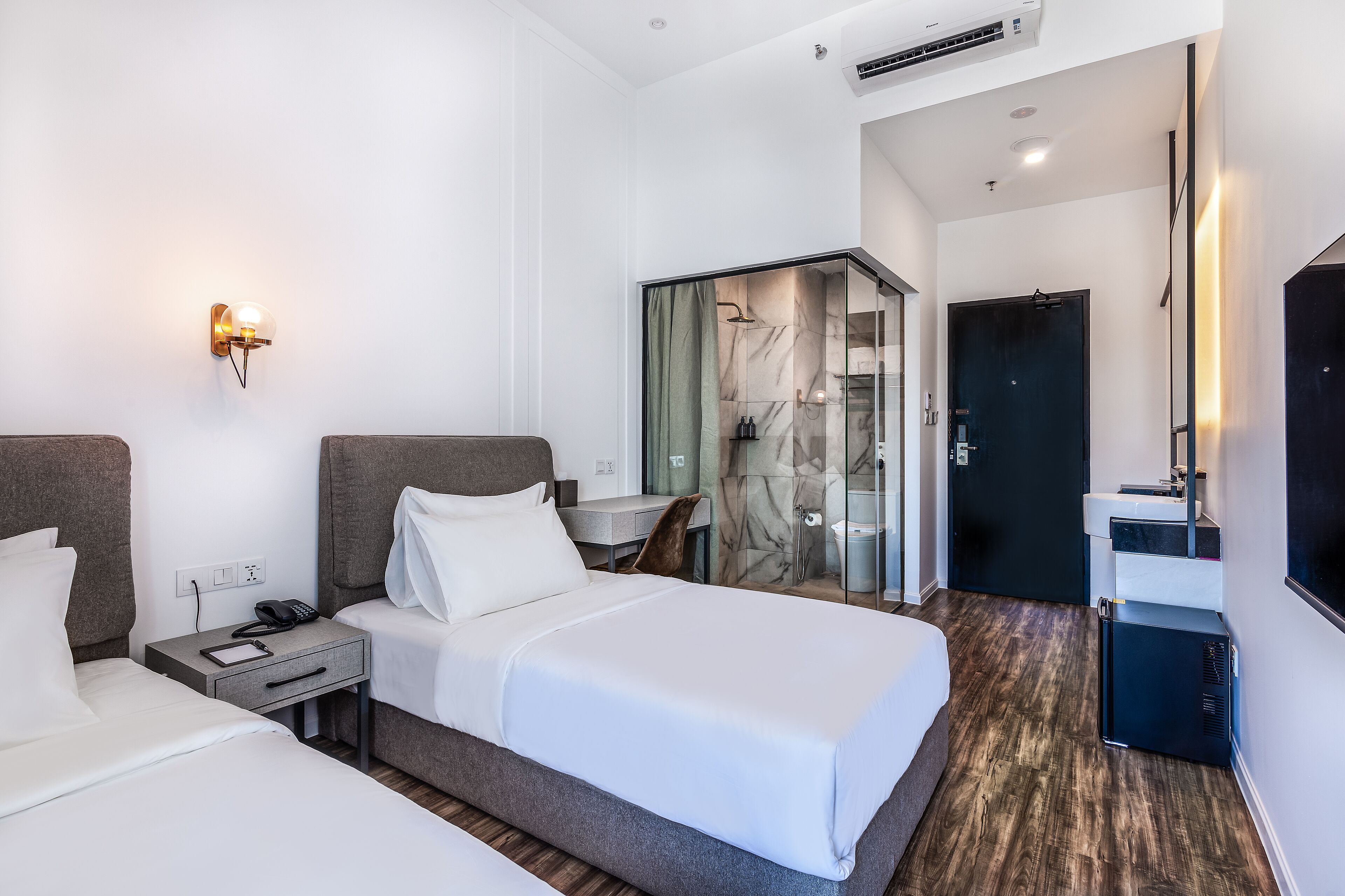A hotel room with a bed, bedside tables, a desk, a shower area, and a TV.