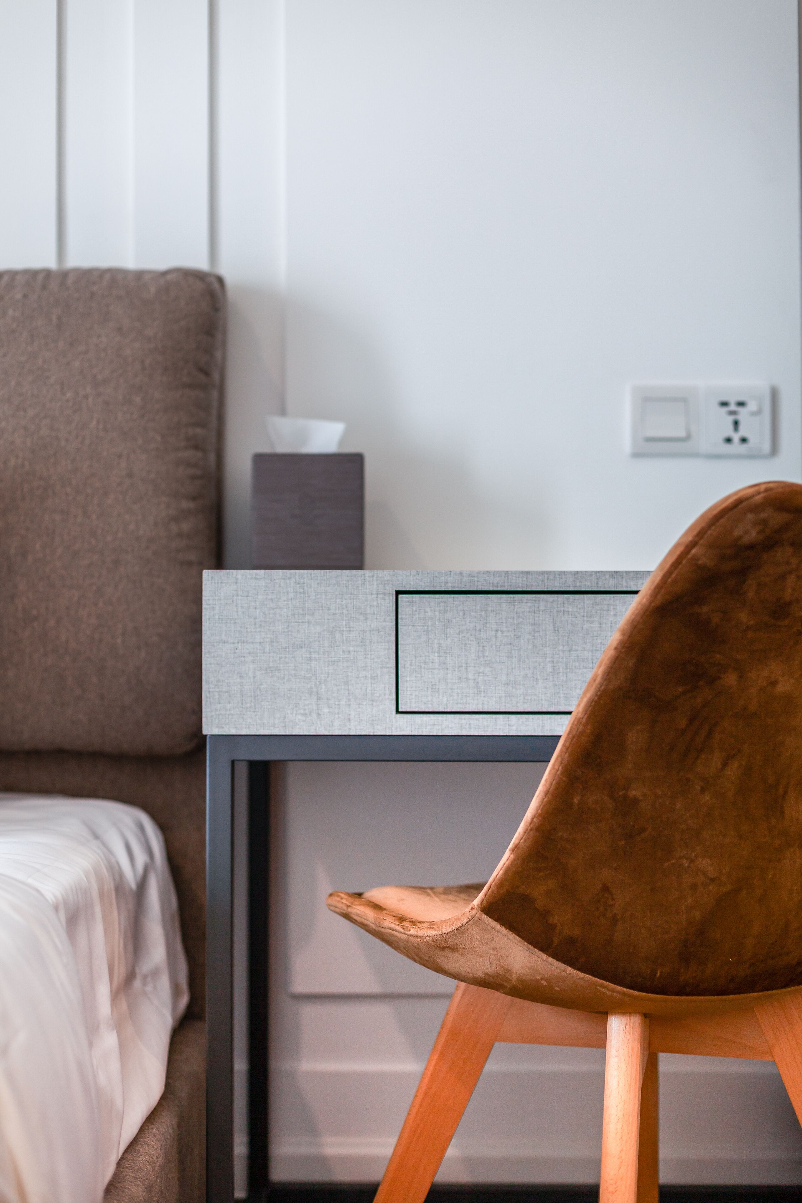 A modern room with a bed, a desk with a chair, and a bedside table.