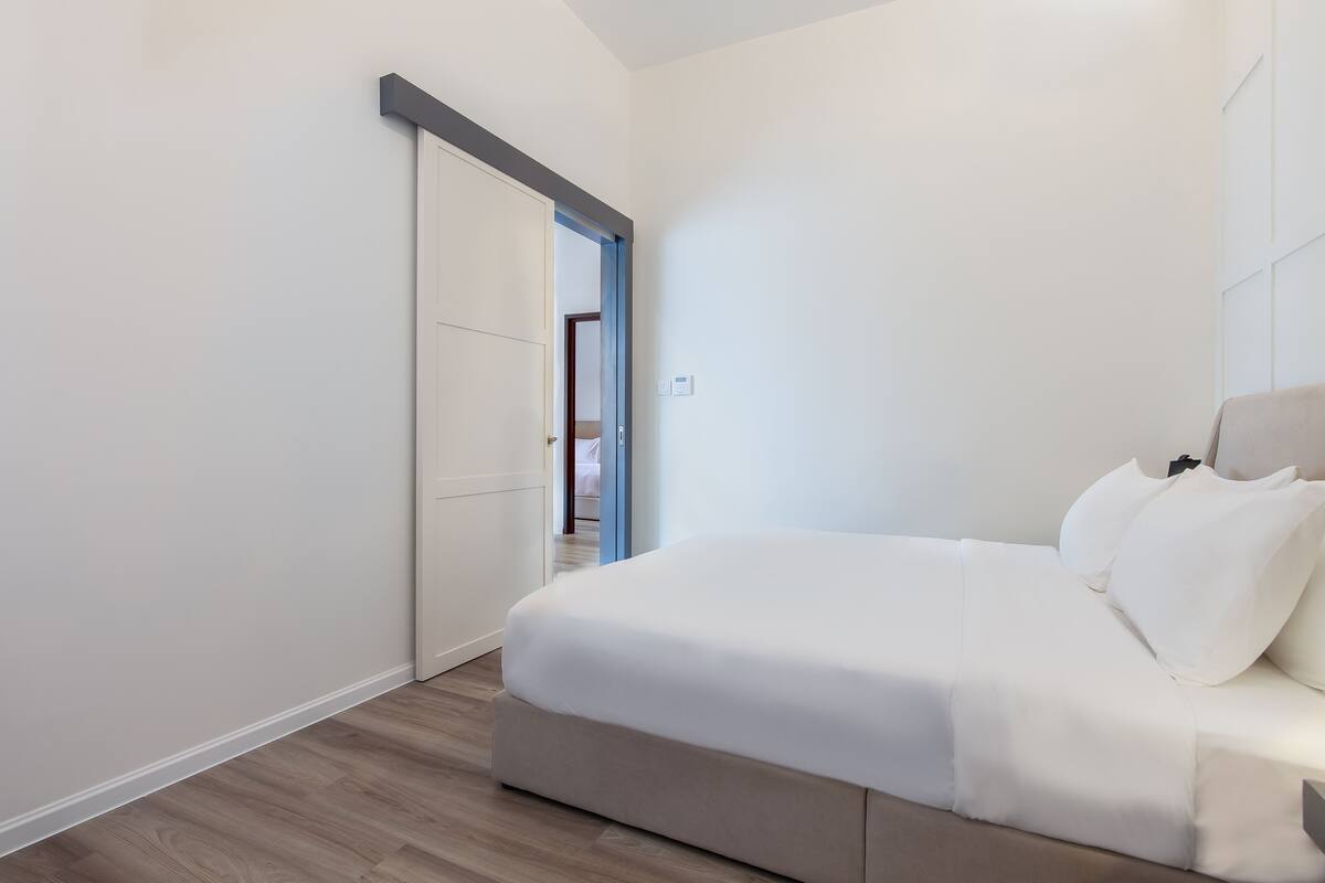 A modern bedroom with a large bed, a sliding door, and a visible bathroom in the background.
