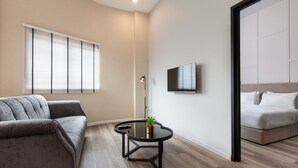 Una sala moderna con sofá, una mesa redonda con una planta, un televisor montado en la pared y una cama en la habitación contigua.