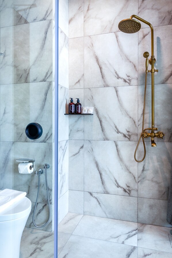 A bathroom with a marble floor, a glass shower enclosure, a gold showerhead, and a white toilet.