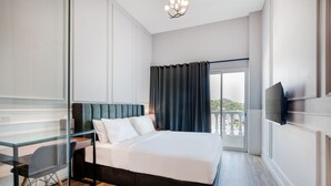 Habitación de hotel moderna con una cama grande, un escritorio con silla, un televisor montado en la pared y un balcón con vistas.