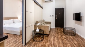 Habitación de hotel con cama, sofá, escritorio con lámpara, televisor y puerta.