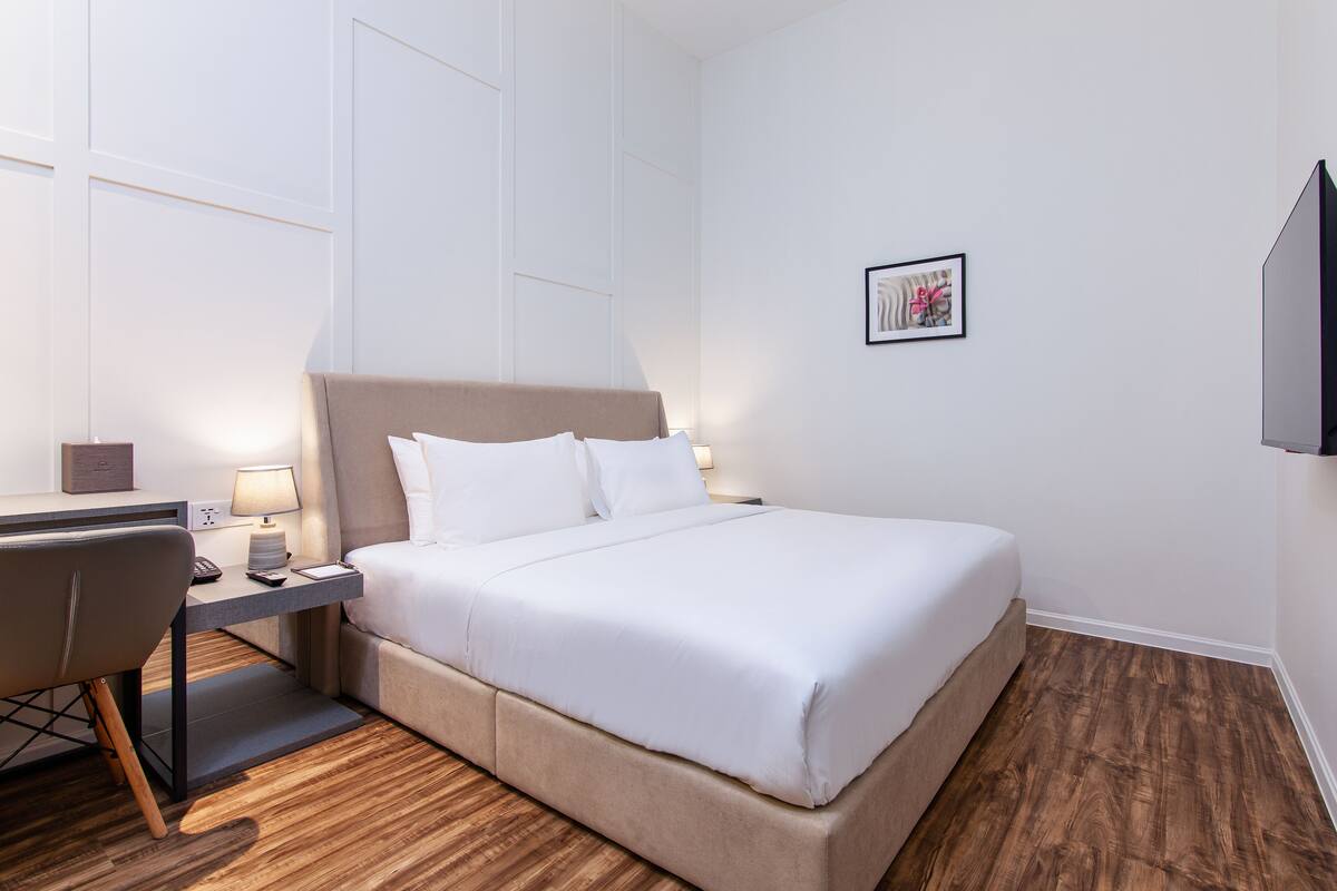A hotel room with a bed, a desk, a chair, a lamp, and a framed picture on the wall.