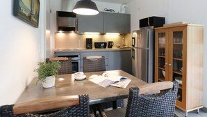 A compact kitchen with a dining table, chairs, a hanging light fixture, a refrigerator, and a cabinet. - Haus am Teich, Whg. D16 (Ostseebad Boltenhagen)