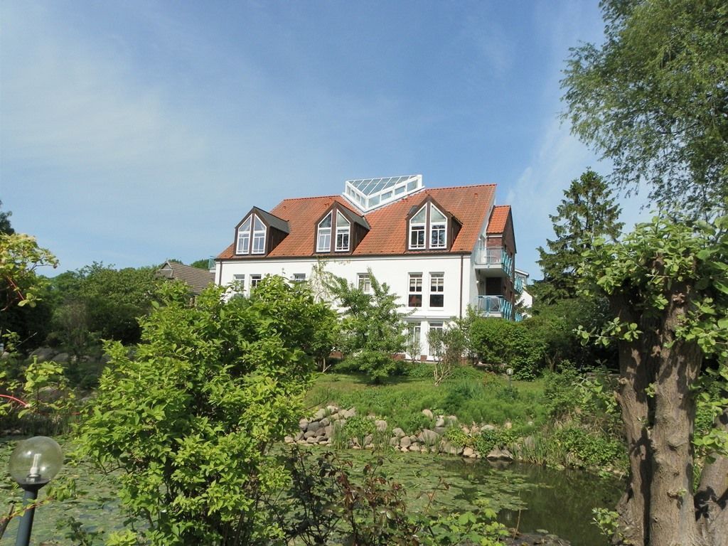 Ein großes, weißes Gebäude mit rotem Dach, umgeben von Grünflächen und einem Teich.