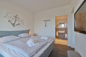 A hotel room with a bed, a nightstand, a wall-mounted towel rack, a bathroom with a sink and mirror, and a framed picture on the wall. - Hafenspitze App. 09, Deutschland (Wismar)