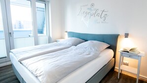 Cama doble con sábanas blancas, cabecera azul claro y mesita de noche con un libro.