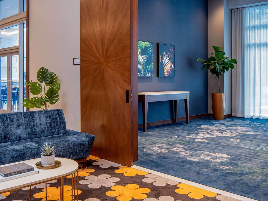 Um hall moderno com um sofá azul, uma mesa de centro com um livro, uma grande planta em vaso e um tapete estampado.