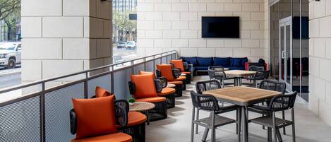 A modern outdoor seating area with orange and black furniture, a flat-screen TV, and a view of the street.