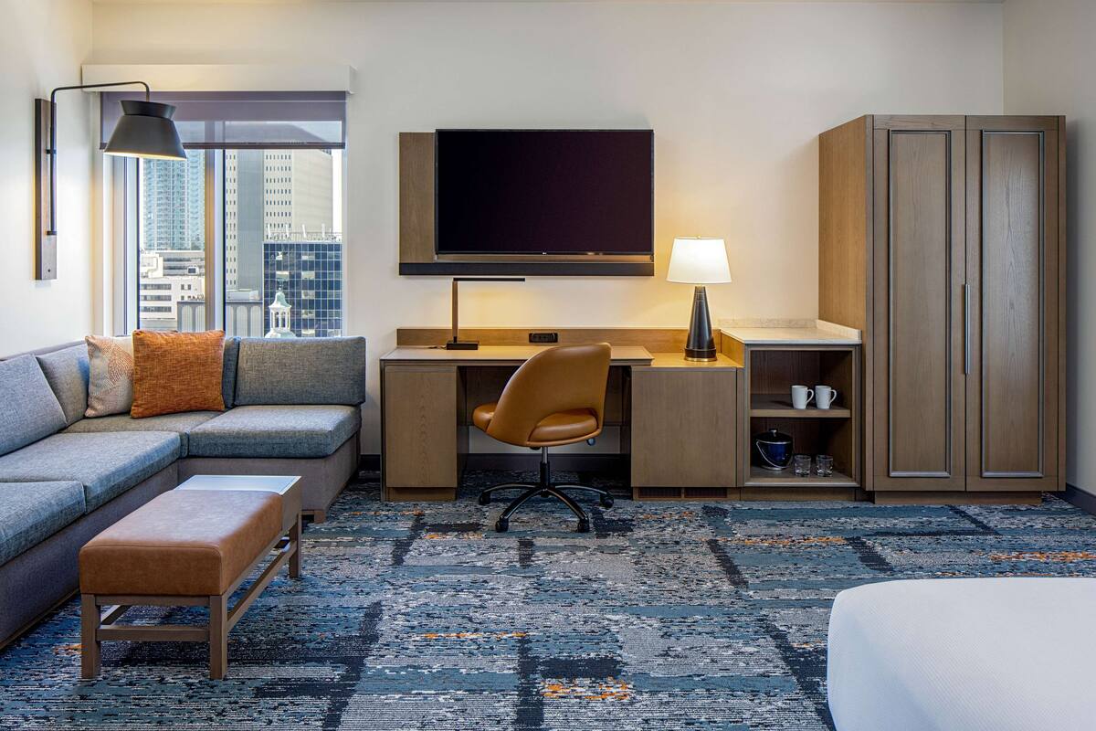 Ein modernes Hotelzimmer mit Sofa, Schreibtisch, Stuhl und Kleiderschrank.