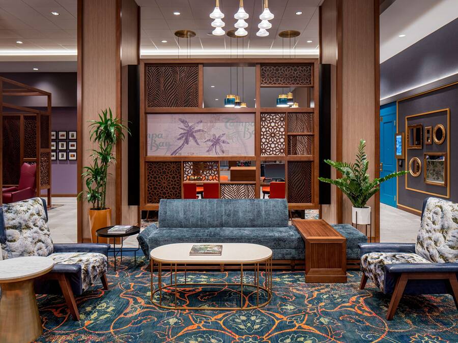 A modern hotel lobby with a blue sofa, two armchairs, a coffee table, and decorative plants.