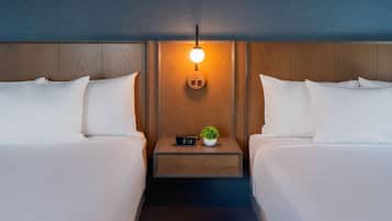Ein Hotelzimmer mit zwei Betten, einem Nachttisch mit einer Uhr und einer kleinen Pflanze sowie einer wandmontierten Lampe.