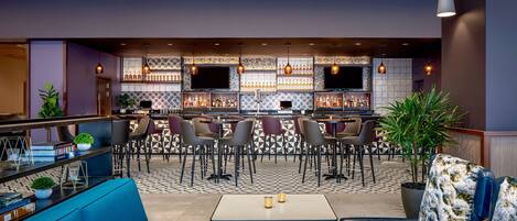 A modern bar area with seating, a bar counter, and a variety of bottles.