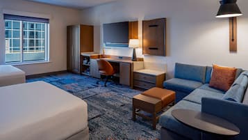 A hotel room with a bed, a desk, a chair, a sofa, a small table, a lamp, and a TV.