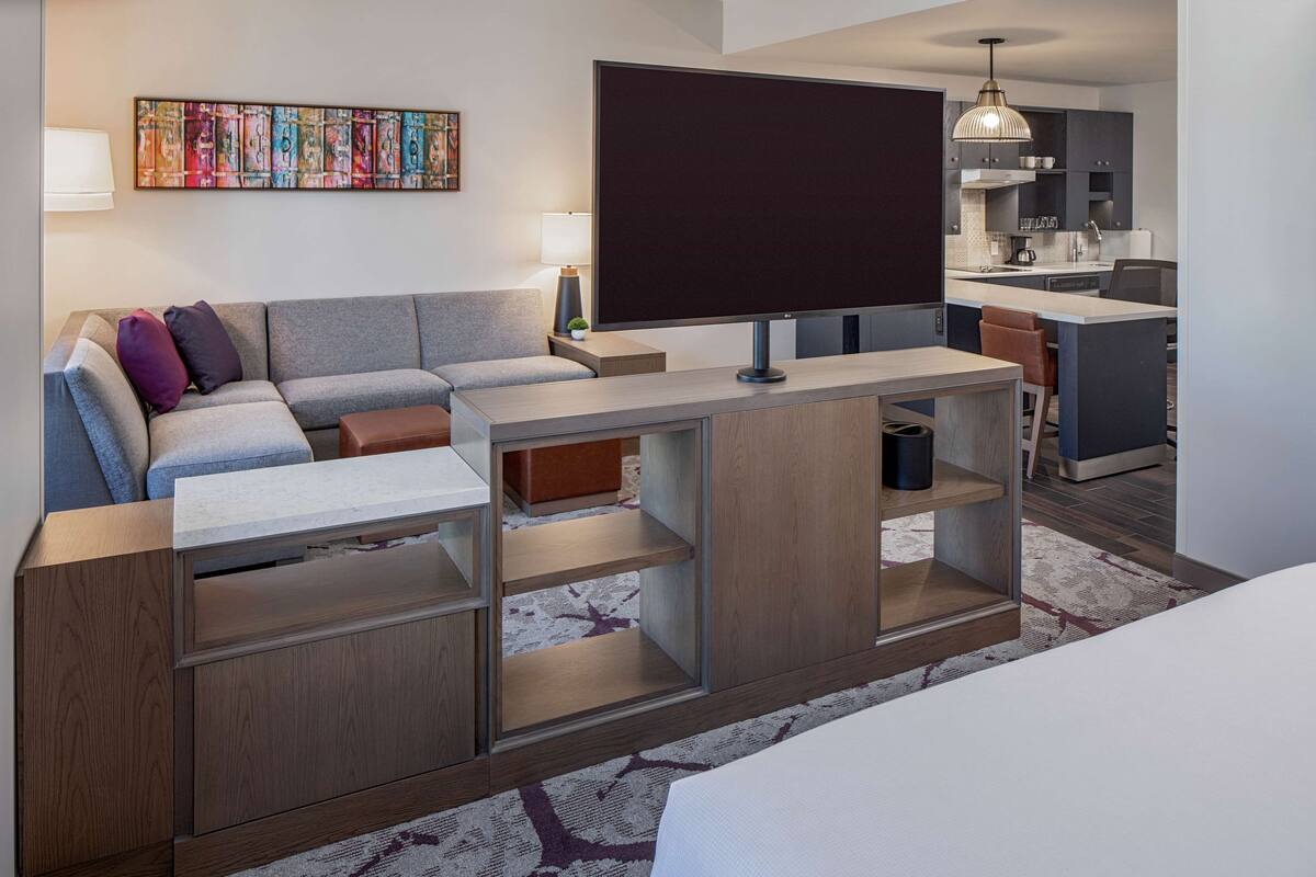 A modern living room with a sectional sofa, a flat-screen TV, and a built-in wooden shelving unit.