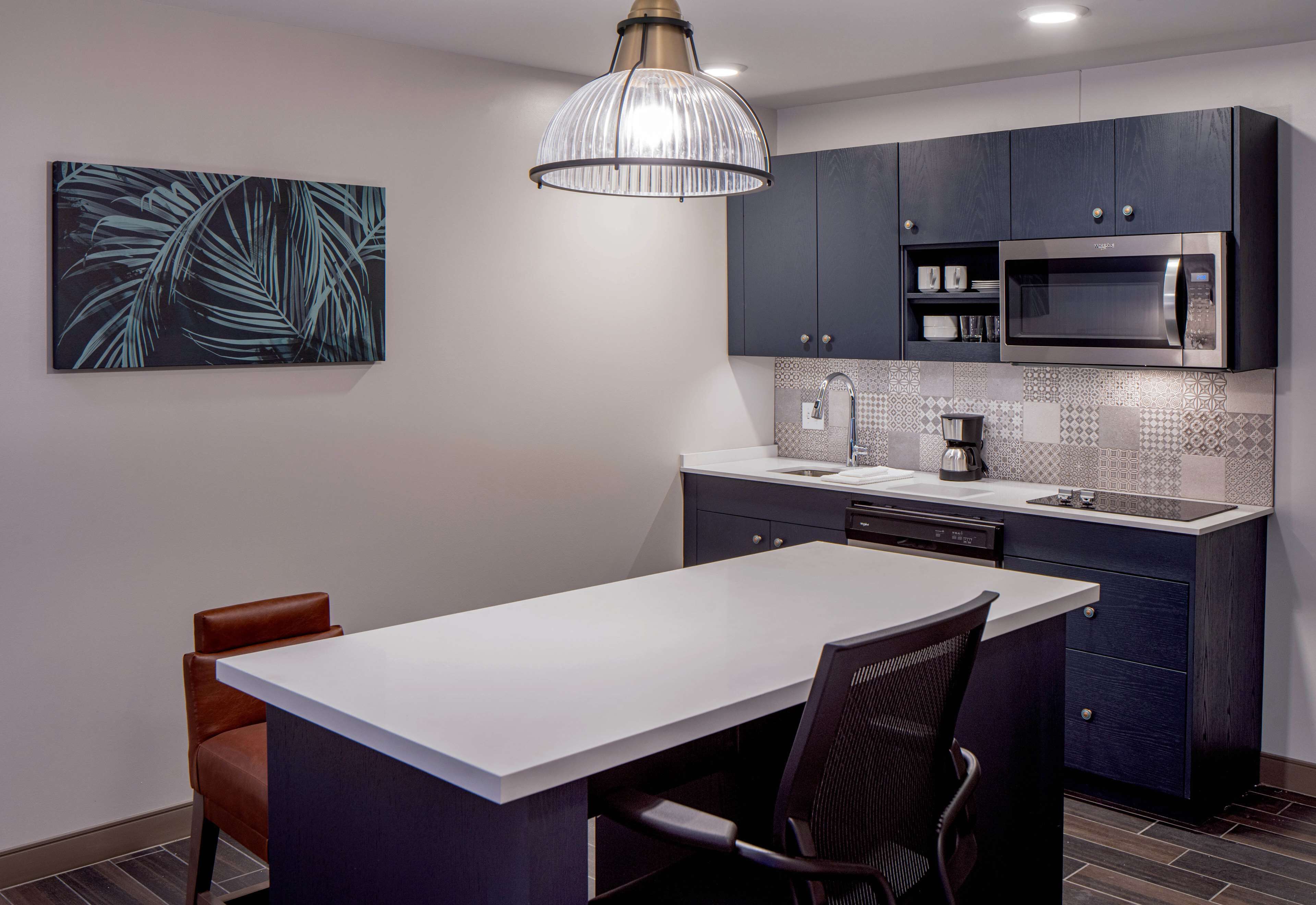 A modern kitchen with dark cabinets, a white countertop, a large island with seating, and a hanging pendant light.