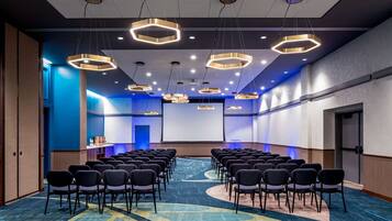 A conference room with rows of chairs, a large screen, and hexagonal ceiling lights.
