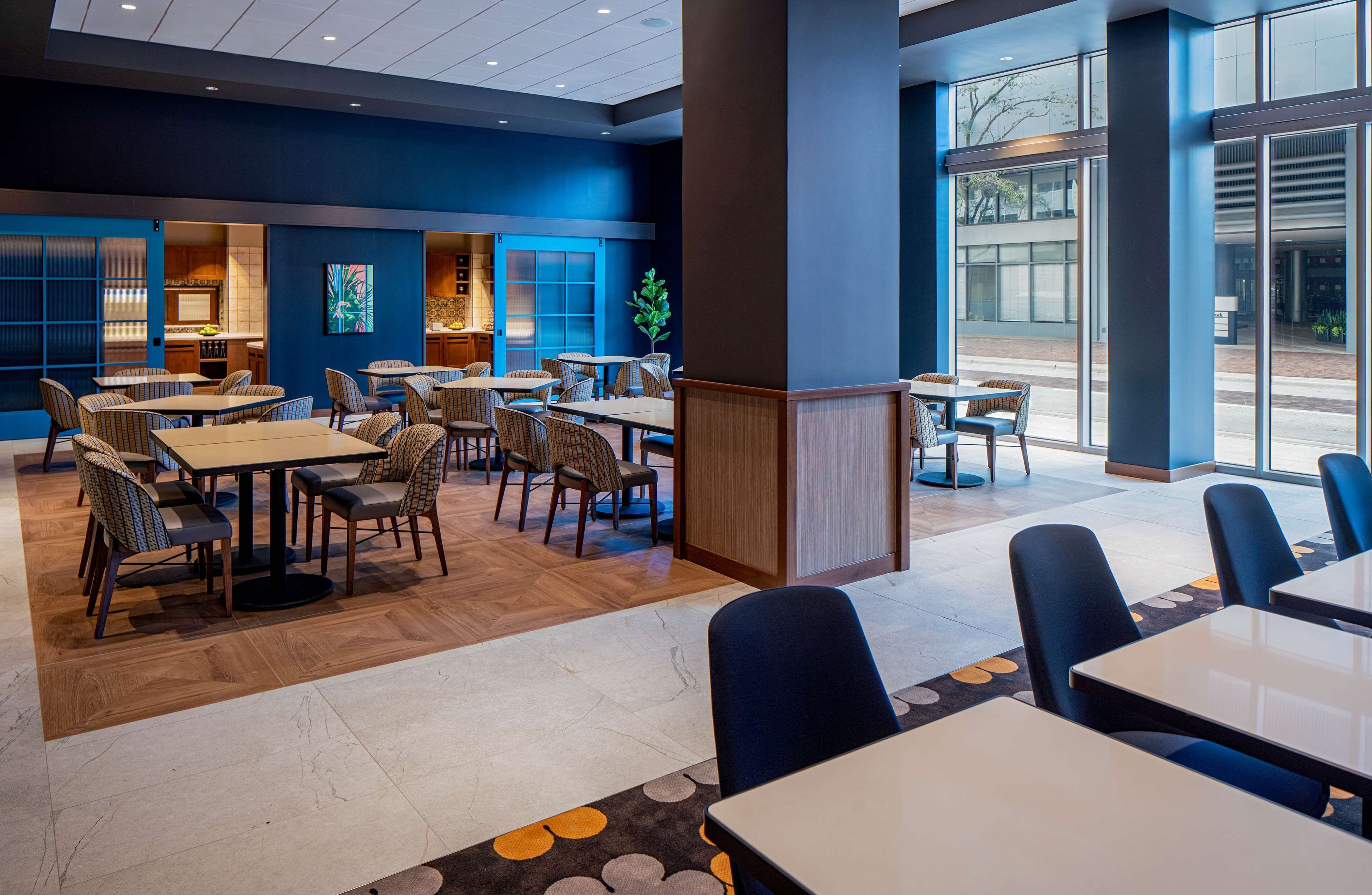 A modern restaurant with multiple dining areas, including booths and tables, and large windows offering views of the outside.
