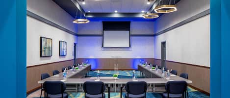 Une salle de conférence avec une longue table, des chaises, un écran de projection et une moquette bleue.