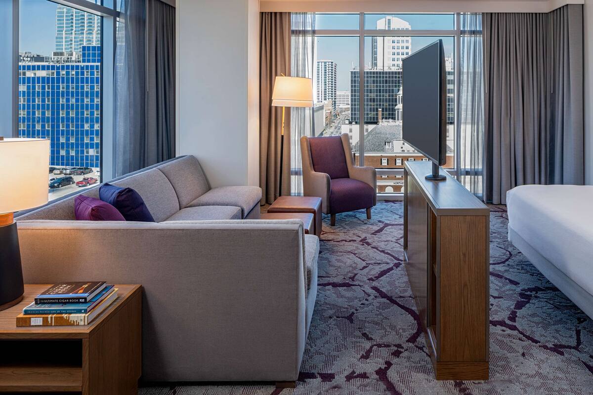 A hotel room with a sofa, armchair, desk, and bed.