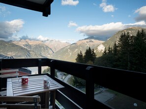 Ein Balkon mit Tisch und zwei Tassen, mit Blick auf eine gebirgige Landschaft mit Bäumen und einer Straße.