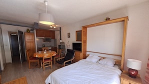 Un dormitorio con cama, mesita de noche, lámpara, cabecera de madera y un escritorio pequeño con silla.
