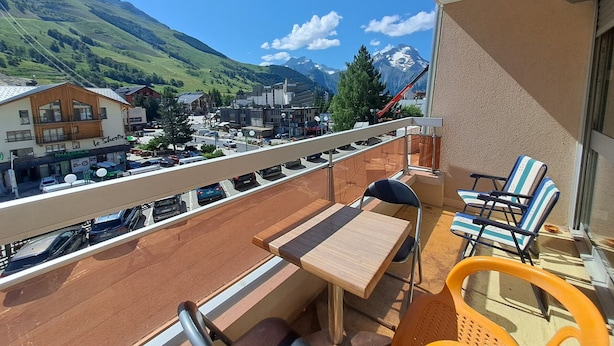Un balcón con una mesa y sillas, con vistas a un pueblo y montañas al fondo.