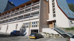 Un edificio de varios pisos con techo plano, una escalera que sube a los pisos superiores y un área de estacionamiento con automóviles.