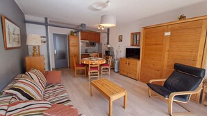 Una sala de estar con sofá, una mesa de centro de madera, un sillón de cuero negro, una mesa de comedor con sillas, una cocina con armarios y electrodomésticos, y un guardarropa de madera.