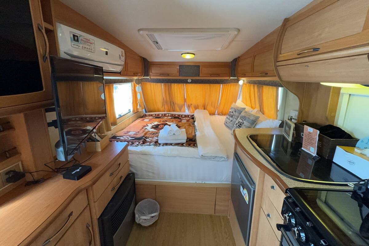 Ein kompaktes Wohnmobil-Interieur mit einer Küchenzeile, einem Bett mit gemustertem Überwurf und einer kleinen Mülltonne.