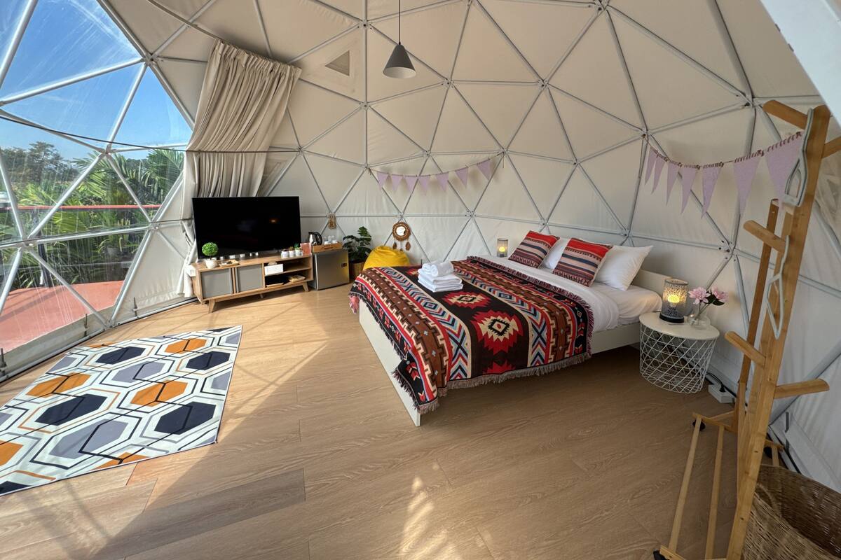 Ein geräumiges Zelt mit einem Bett, einem Fernseher und einem kleinen Tisch mit einer Lampe.
