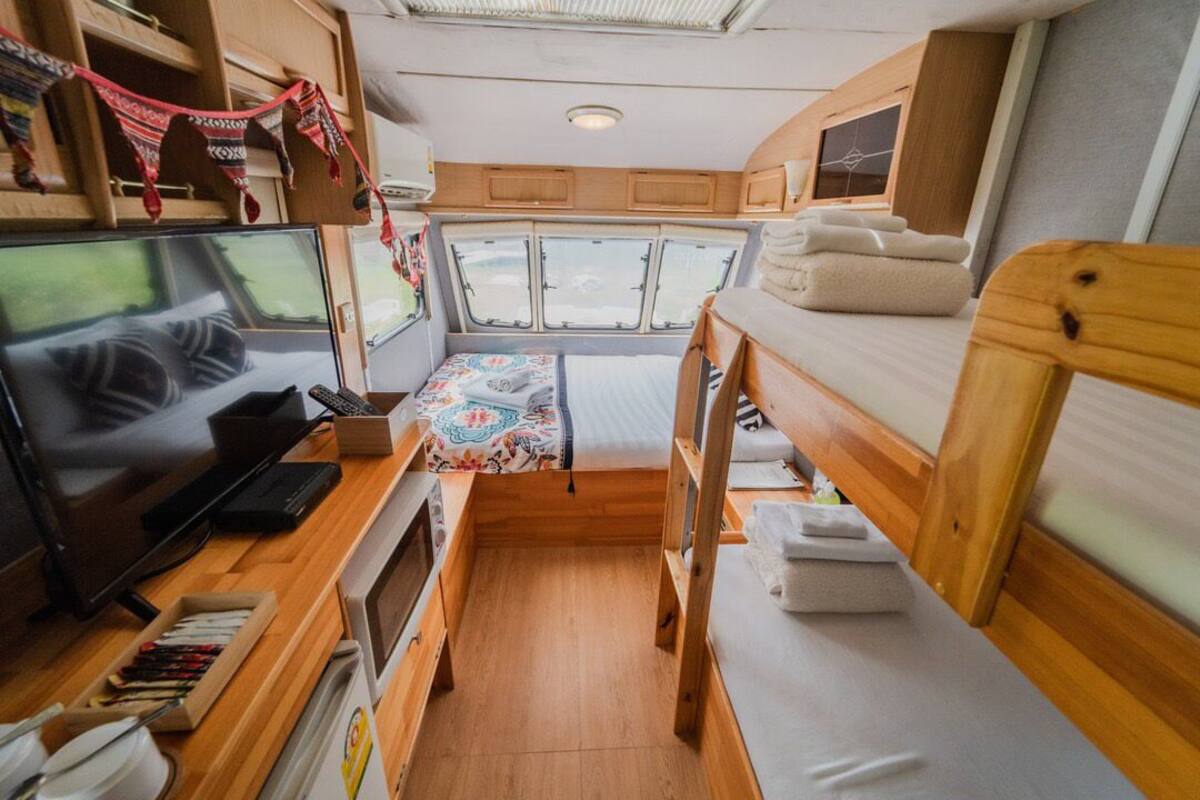 Ein kompaktes Wohnmobil-Interieur mit Bett, Fernseher, kleiner Küchenzeile und einem Fenster für natürliches Licht.