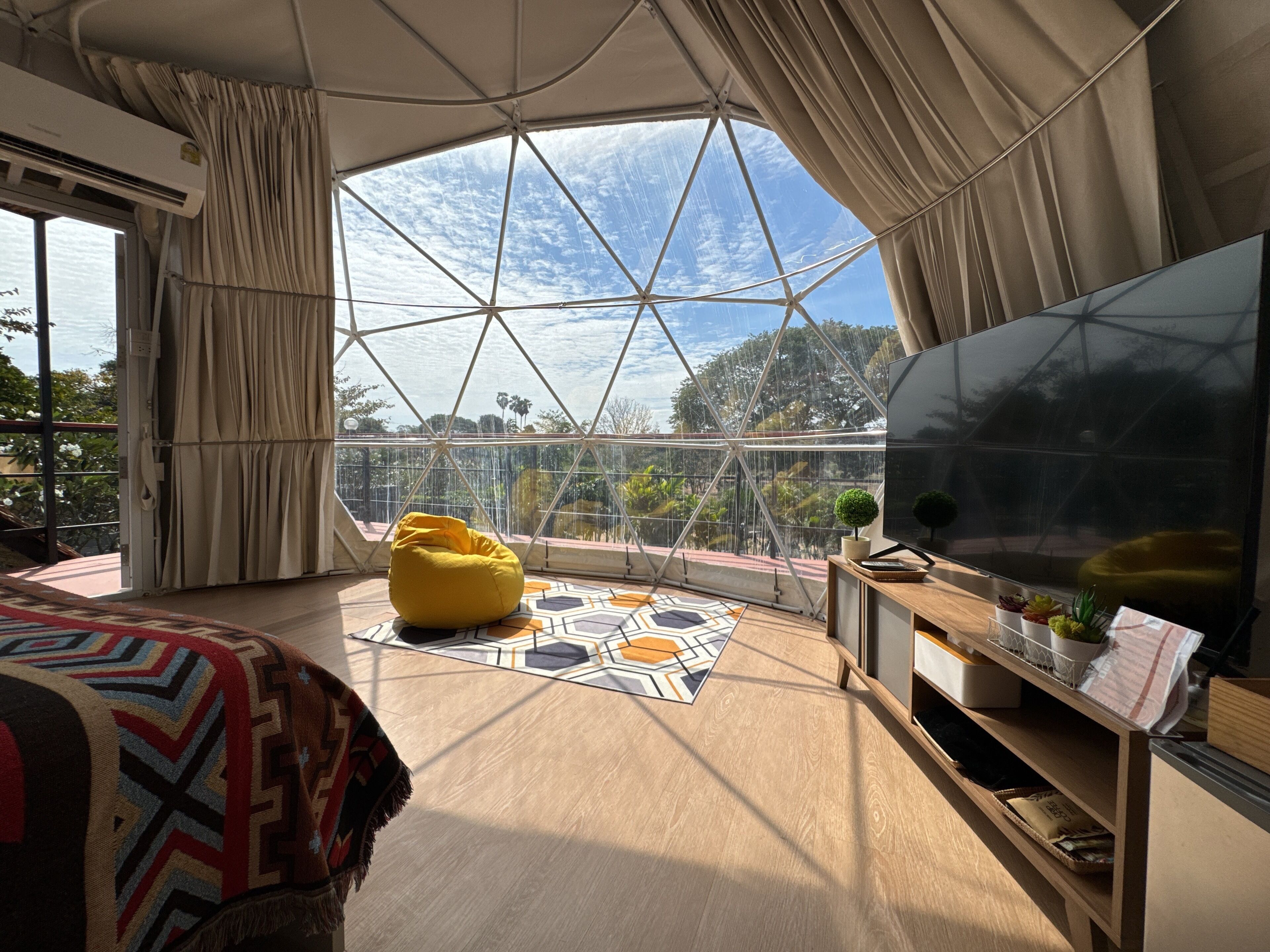 Una habitación amplia con un gran ventanal, un sillón de mezcla amarilla, un televisor de pantalla plana y suelo de madera.