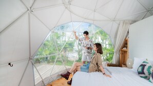 A tented room with a bed, a wooden floor, and a view of greenery outside.