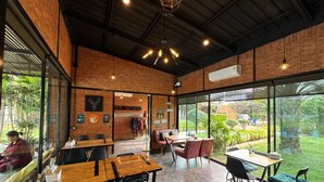 A restaurant with brick walls, large windows, and a mix of wooden and metal furniture.